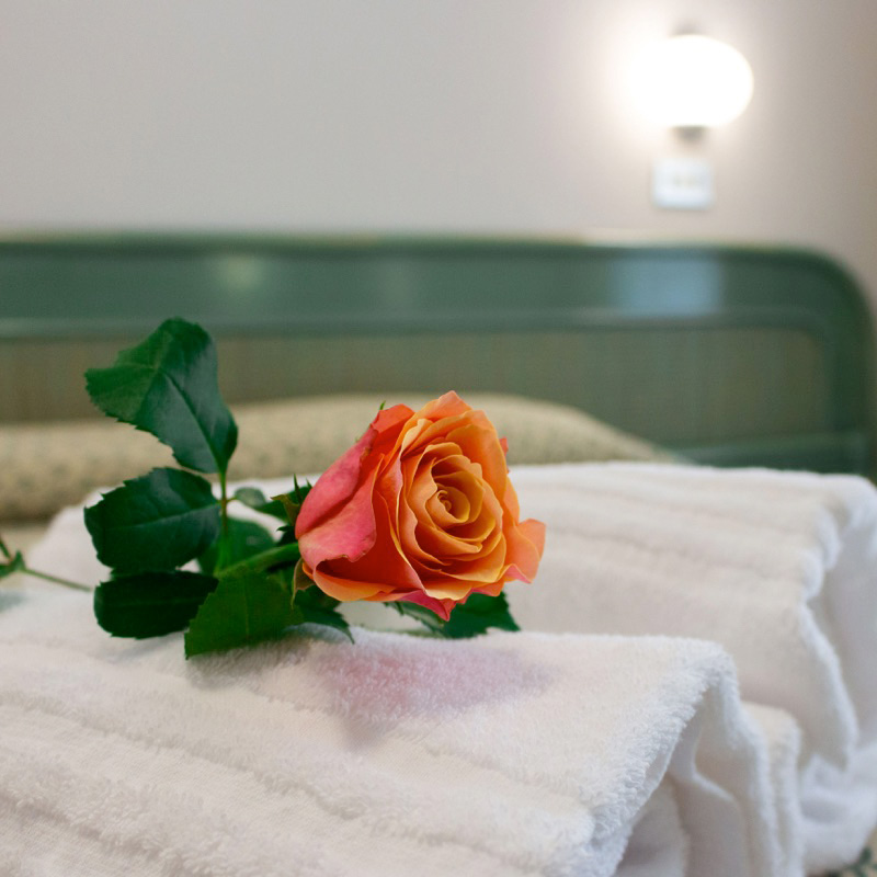 Asciugamani bianchi su un letto con una rosa arancione, testiera verde e luce soffusa sullo sfondo.